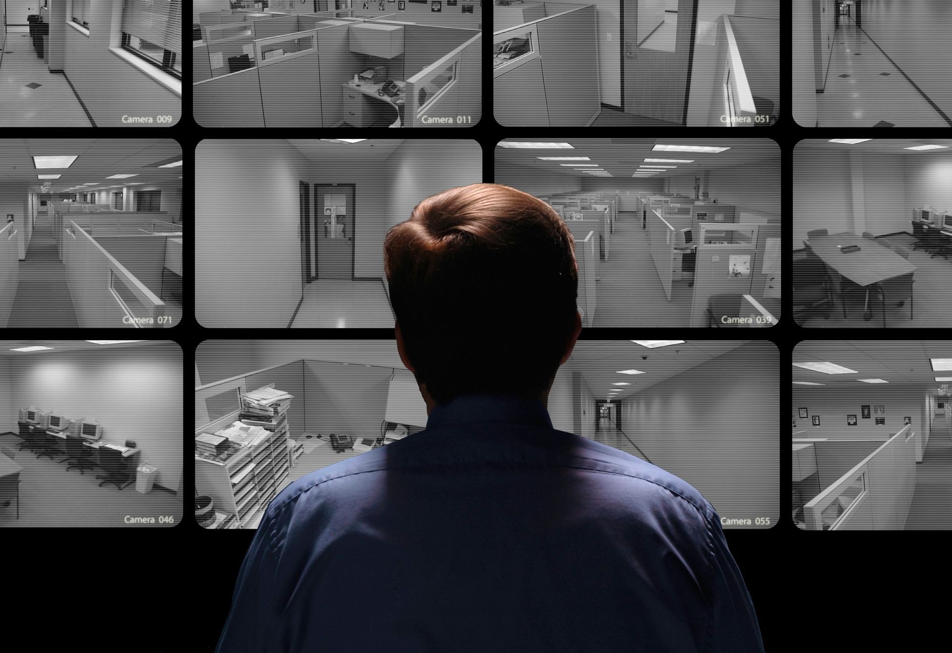 Man in blue shirt watches multiple security camera feeds on a monitor.