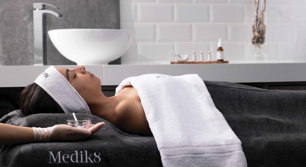 Person receiving a spa facial treatment on a massage table in a modern bathroom spa setting
