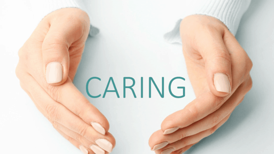 Hands forming a heart around the word “CARING” on a light background