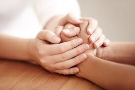 Two hands clasped together in a supportive gesture on a wooden table