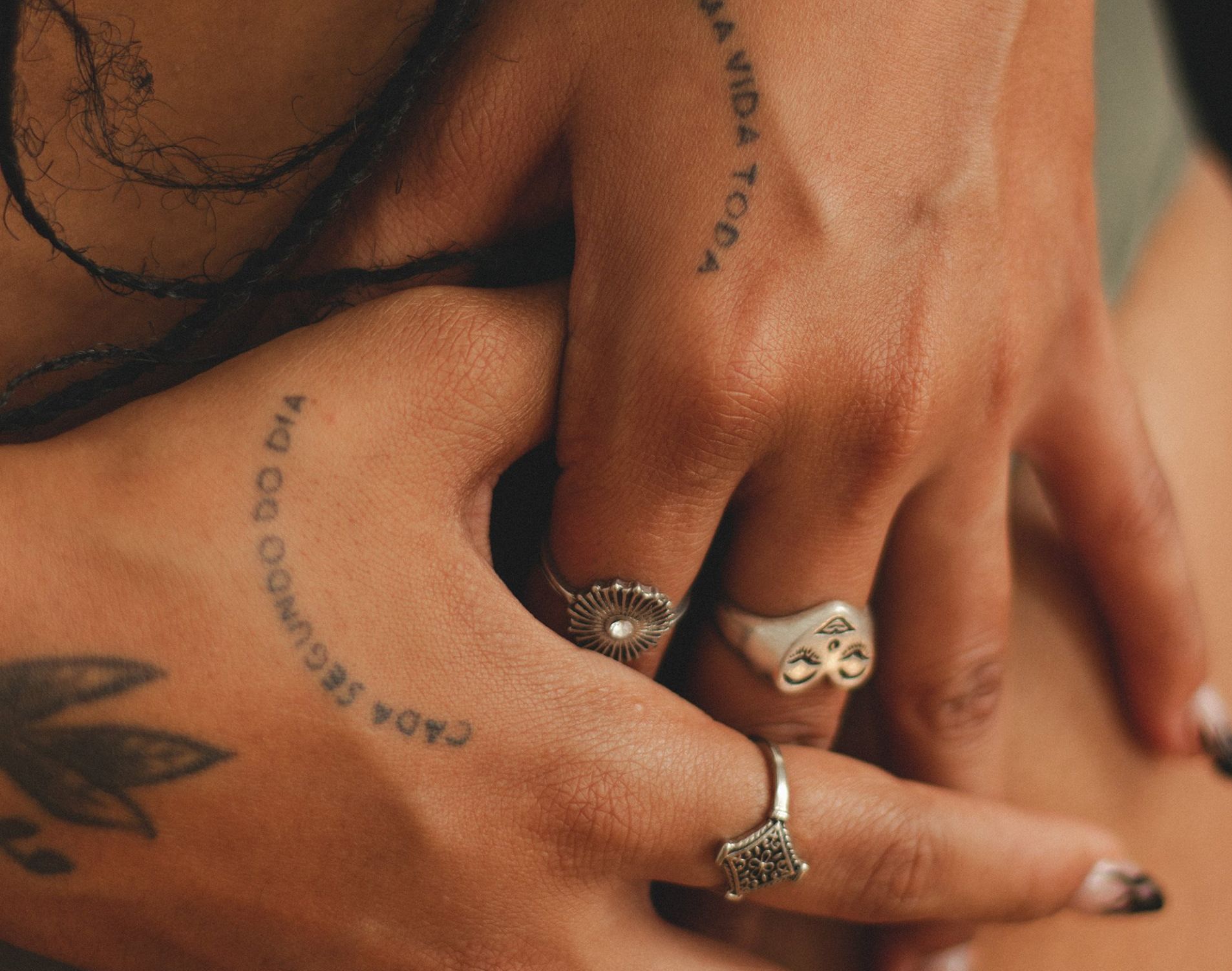 Hands with rings and tattoos touching in a warm close-up shot.