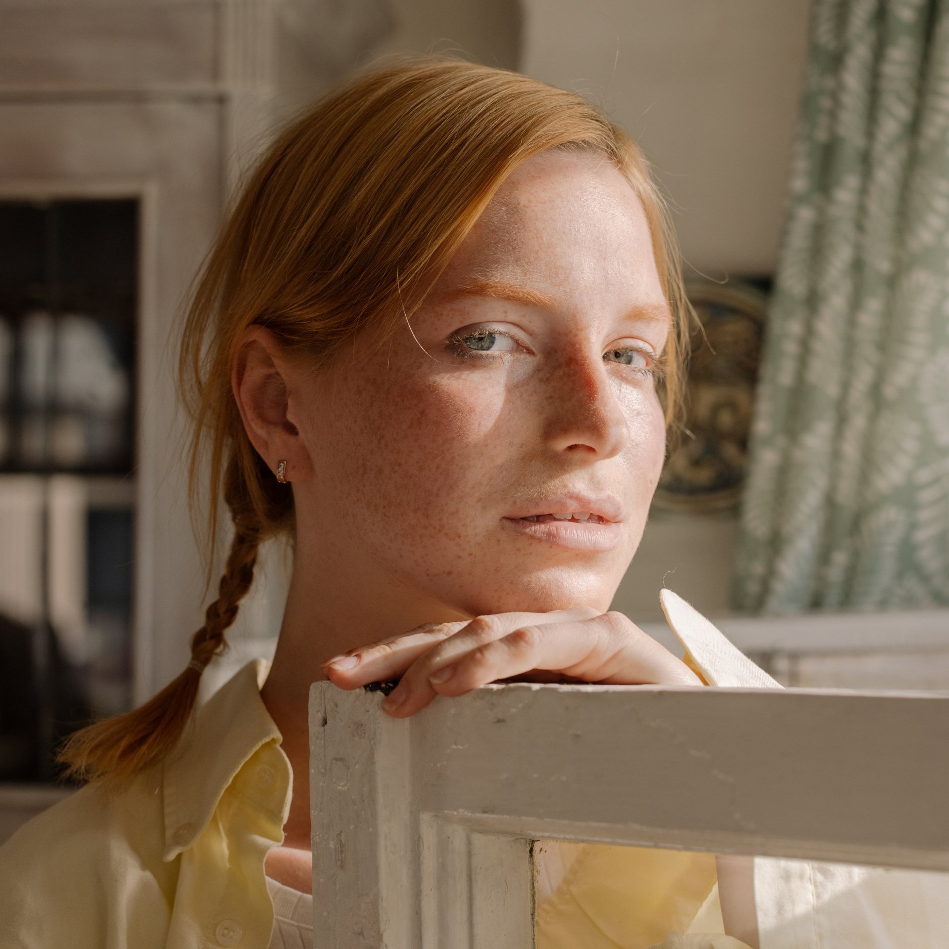 Close-up of a red-haired person resting their chin on a chair, looking toward the camera in warm light.
