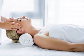 Person receiving a facial massage while lying on a bed with a rolled towel under the head