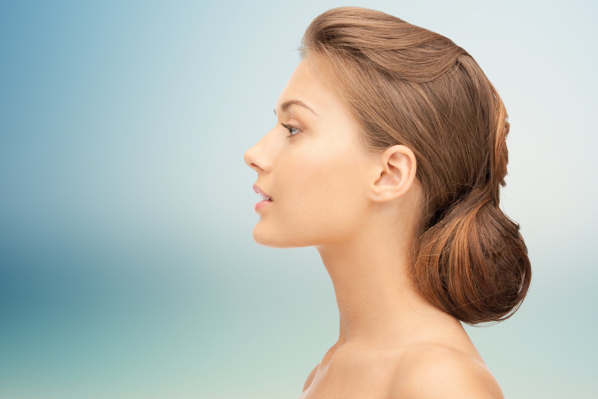 Profile of a woman with a low bun against a soft blue gradient background