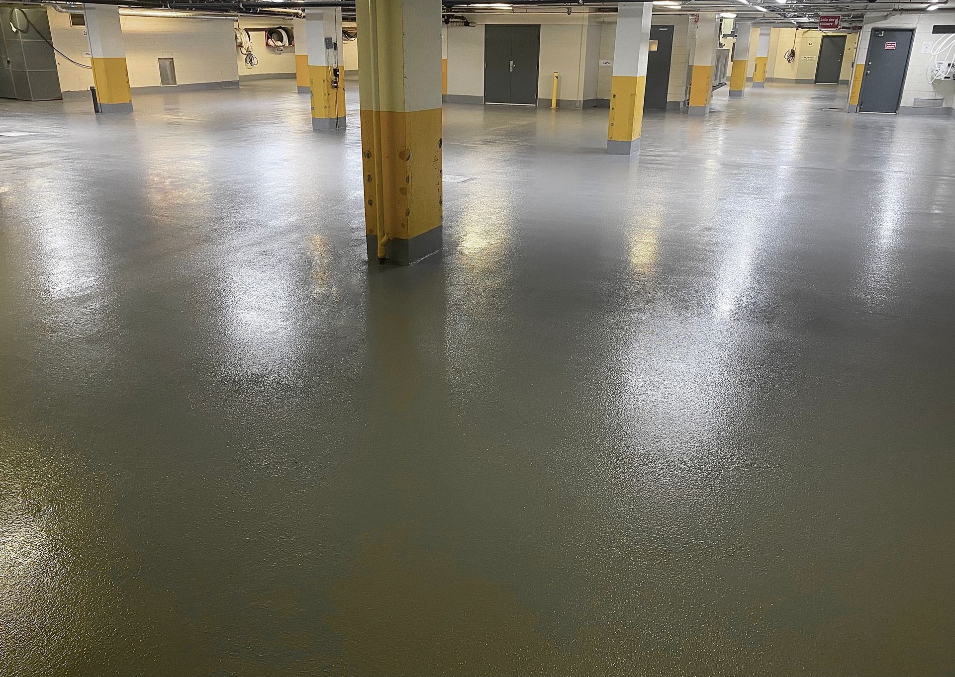 L'intérieur d'un parking souterrain avec un sol gris clair moucheté et brillant et des piliers dont la base est peinte en jaune.