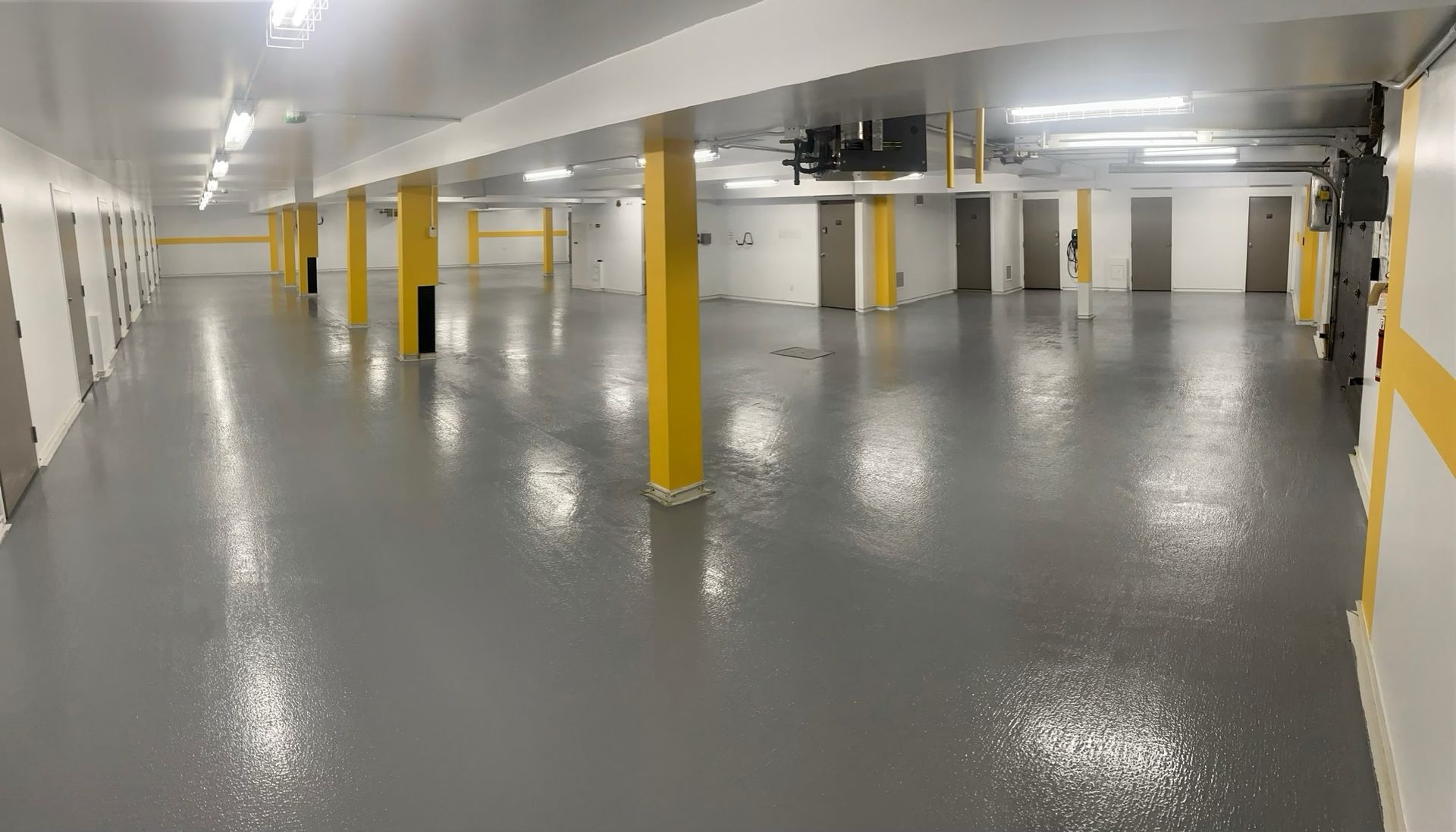 Un sous-sol vide et lumineux, avec un sol en époxy gris brillant, des murs blancs et une rangée de colonnes de soutien jaunes.