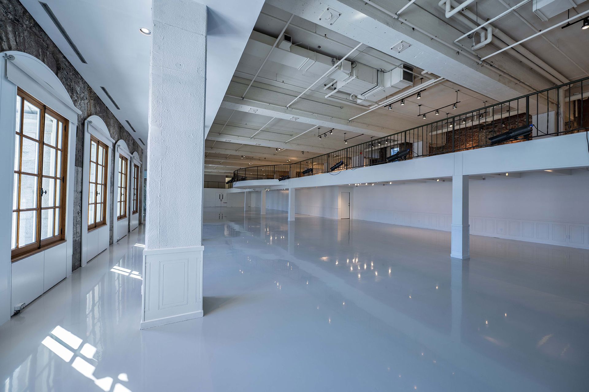 Bright, empty interior space with reflective white floor, large windows, and exposed ceiling structures.