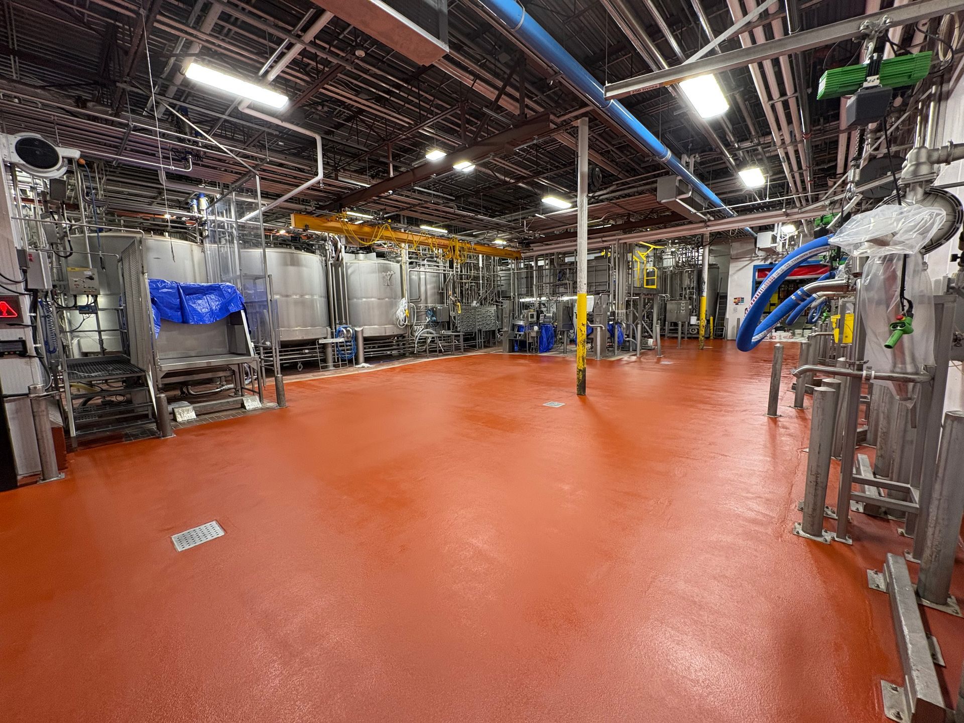 Vue grand angle d'une installation de traitement industriel propre, avec de grandes cuves en acier inoxydable et un sol en époxy rouge.