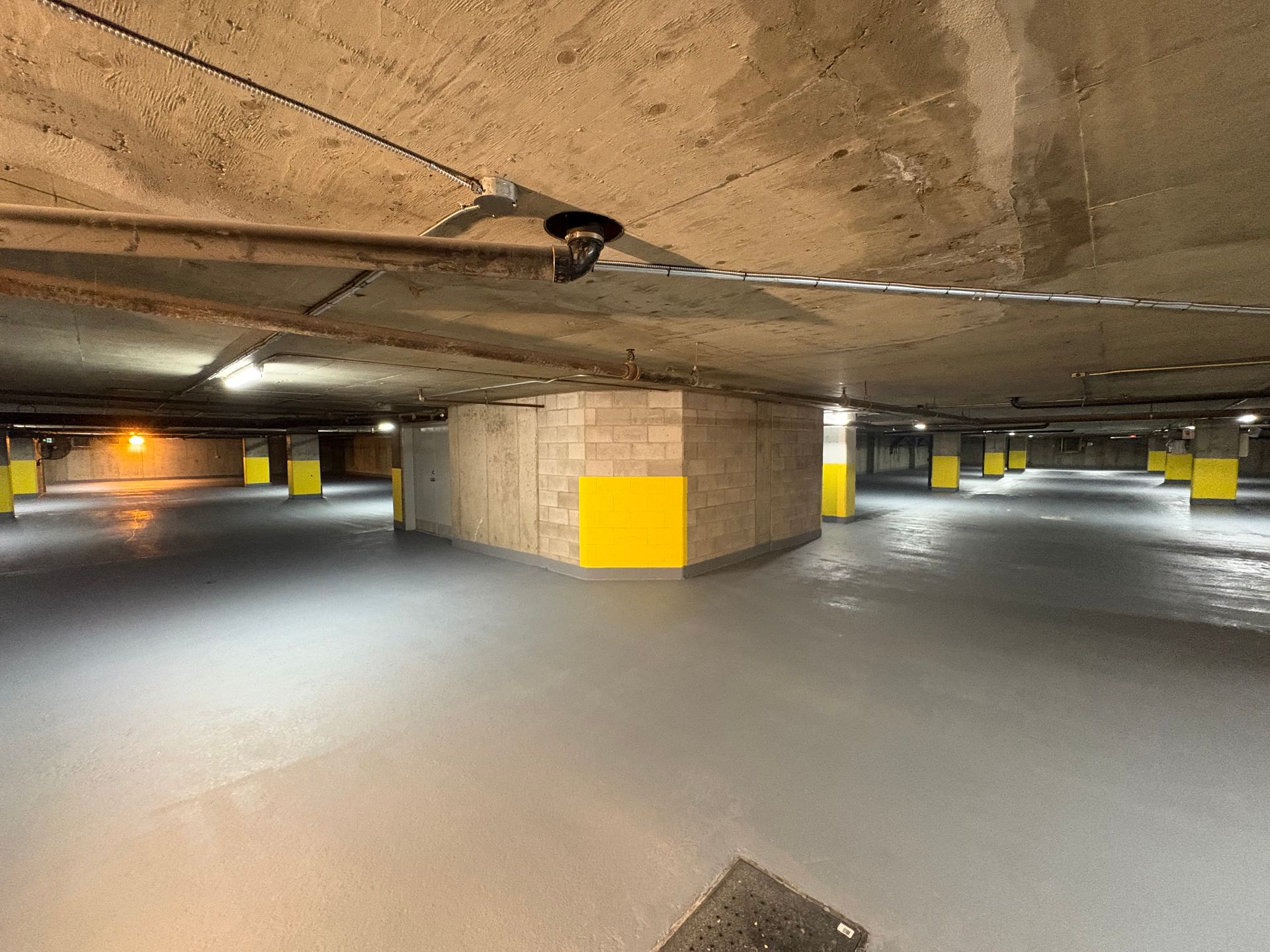 Underground parking garage with gray floor, yellow support pillars, and a concrete ceiling.