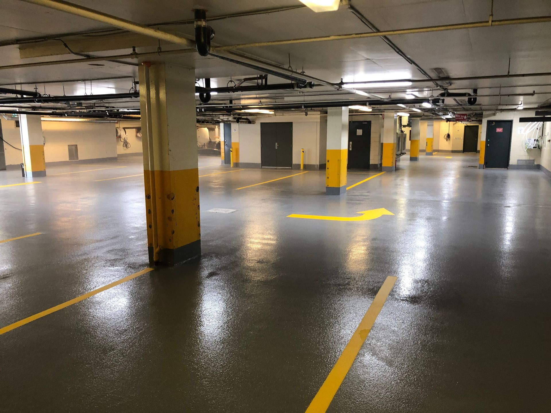 Empty, wet, underground parking garage. Yellow painted support columns and directional arrows on the floor.