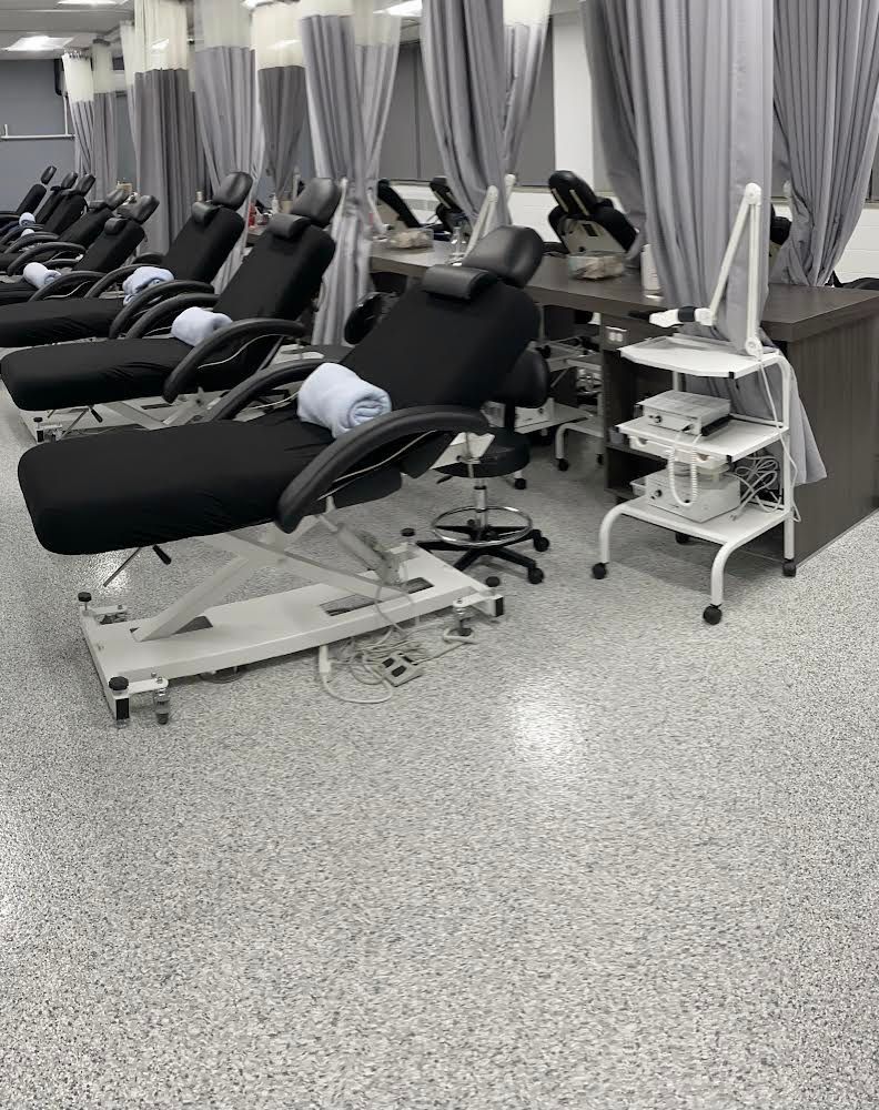 Rows of black treatment chairs in a beauty clinic. Gray curtains and a white wheeled cart are in the space.