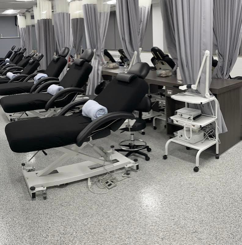 A row of black treatment chairs in a clinic room, each with a towel; gray curtains and gray flooring.