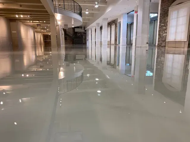 Dans un hall spacieux et moderne, un sol blanc poli et brillant reflète les rangées de piliers blancs et l'éclairage intérieur.