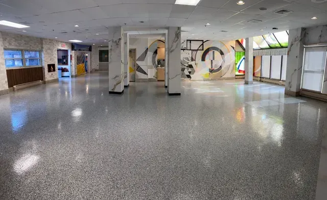 Grand hall vide avec sol moucheté, colonnes blanches et œuvres d'art murales colorées.
