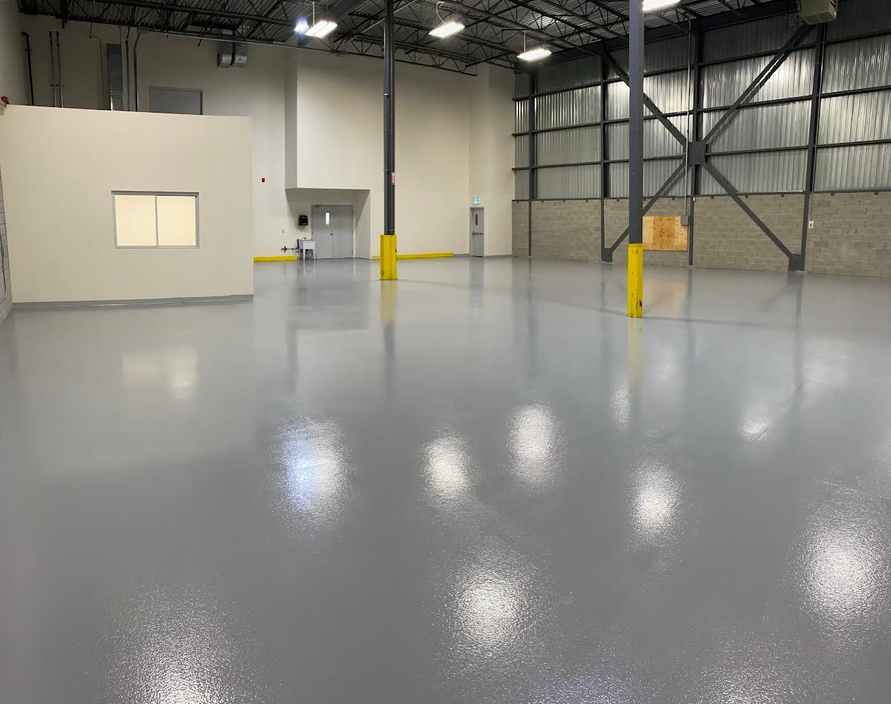 Empty industrial warehouse with a shiny gray epoxy floor. Yellow support beams and high ceiling.