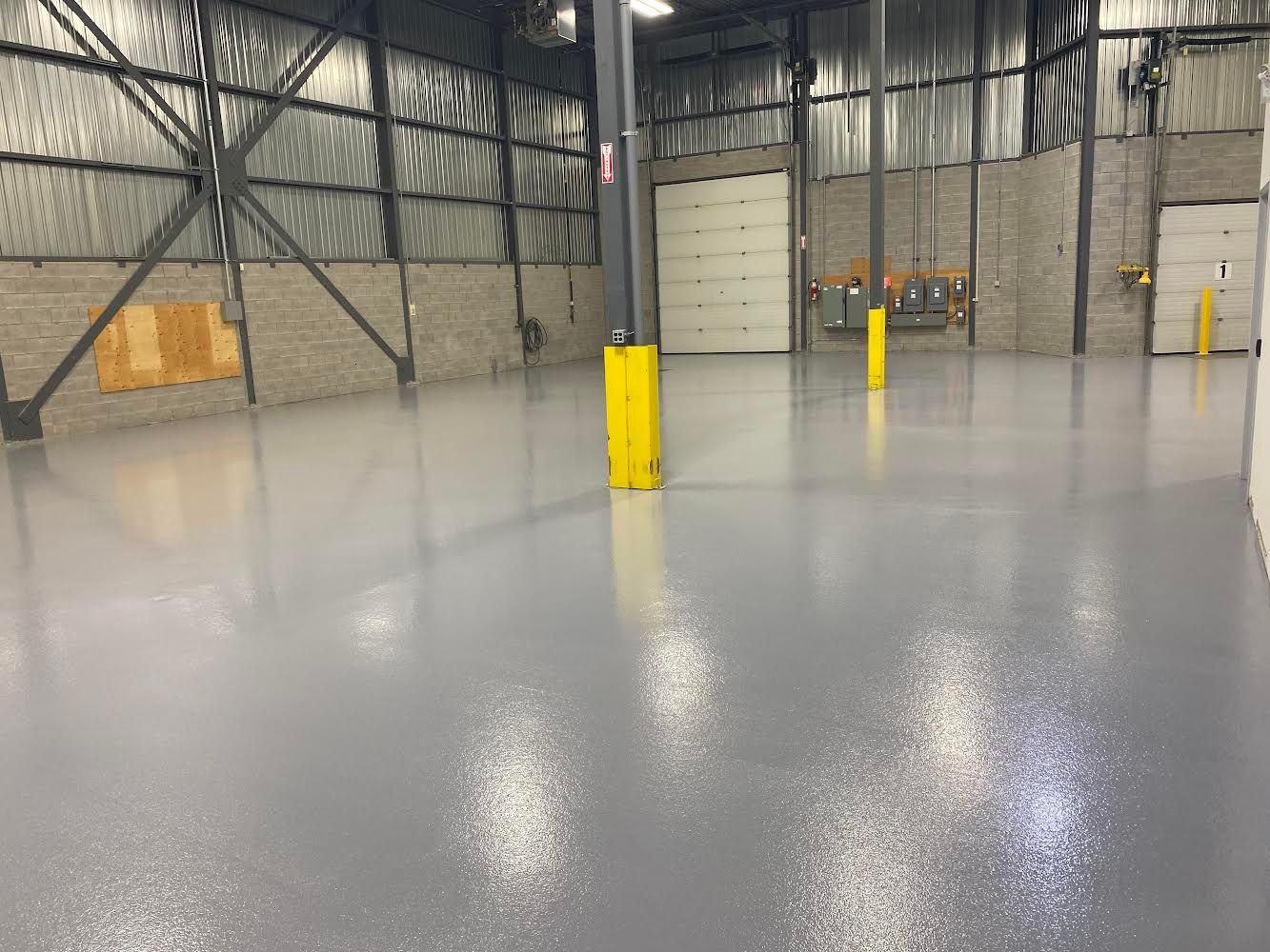 A large warehouse with a gray floor and yellow poles.