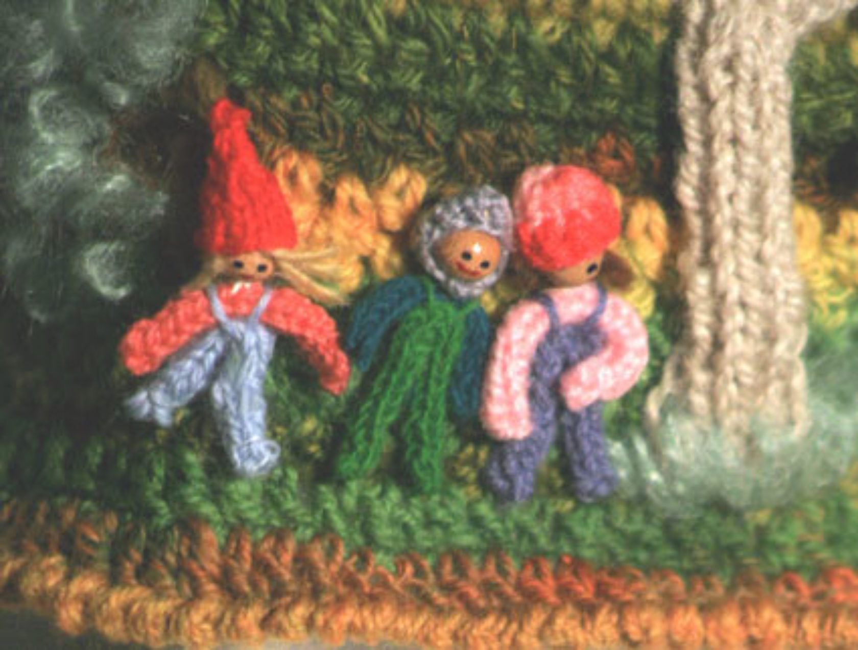Three crocheted gnomes are standing next to each other in a forest.
