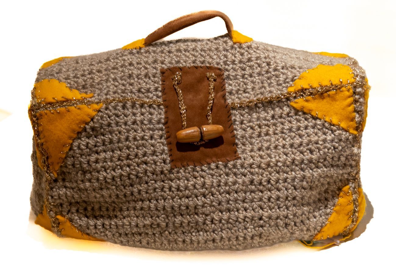 A gray and yellow crocheted bag with a leather handle on a white background.