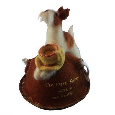 A stuffed dog sits on top of a teapot that says tea tastes better with a tea brush