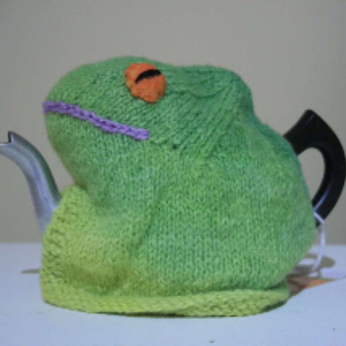A green teapot with a stuffed frog on top of it