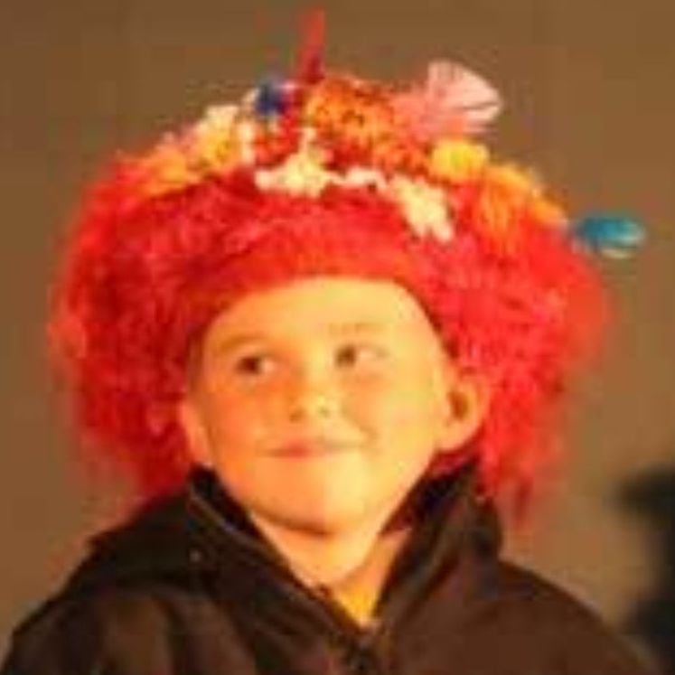 A young boy wearing a red wig with flowers on it.