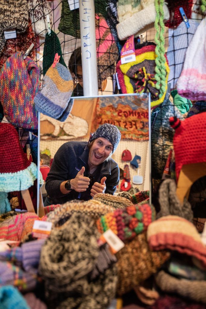 A man is giving a thumbs up in front of a mirror surrounded by hats.