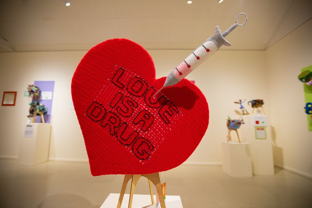 A red heart with a syringe sticking out of it that says love is a drug.
