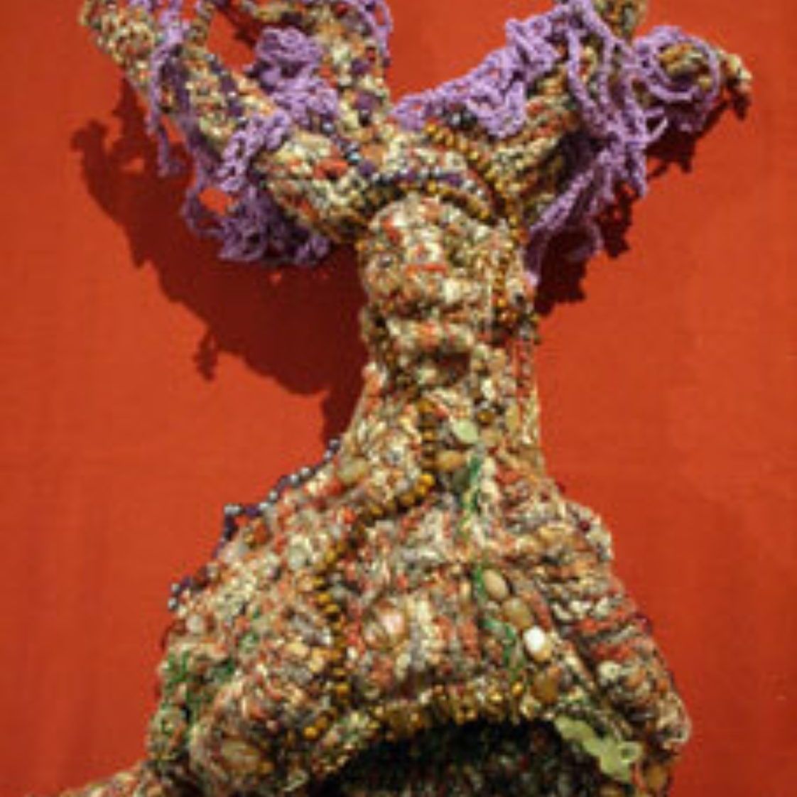A colorful sculpture of a rabbit with purple hair is against a red background.