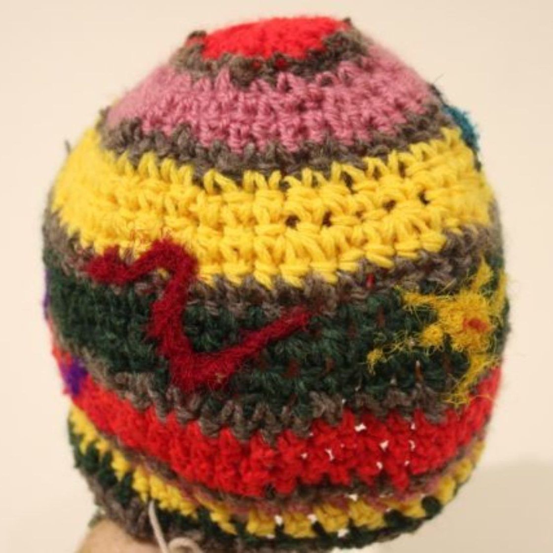 A person is holding a colorful crocheted hat with a heart on it