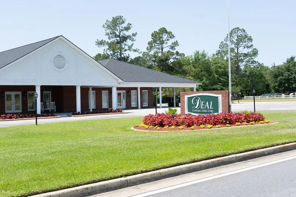 Deal Funeral Home: brick building with sign, green grass, and red flowers.
