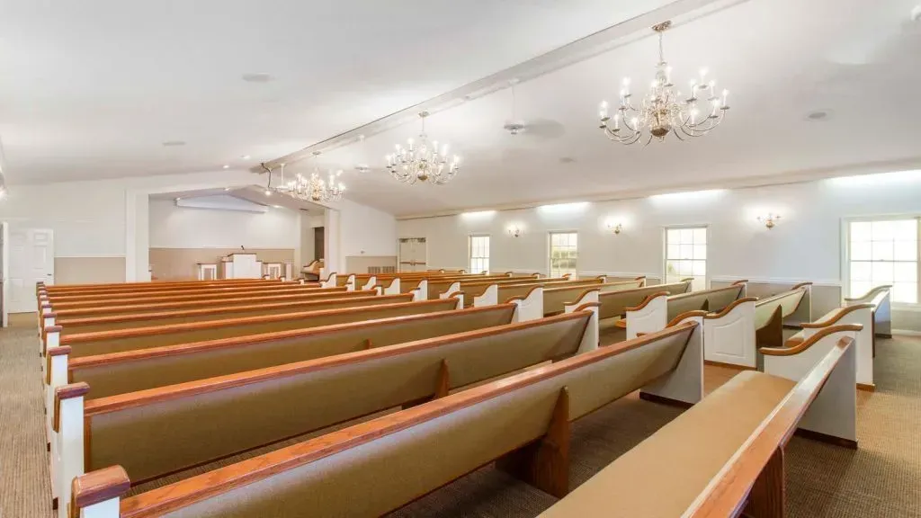Interior view of a light-filled church sanctuary with rows of pews and chandeliers.