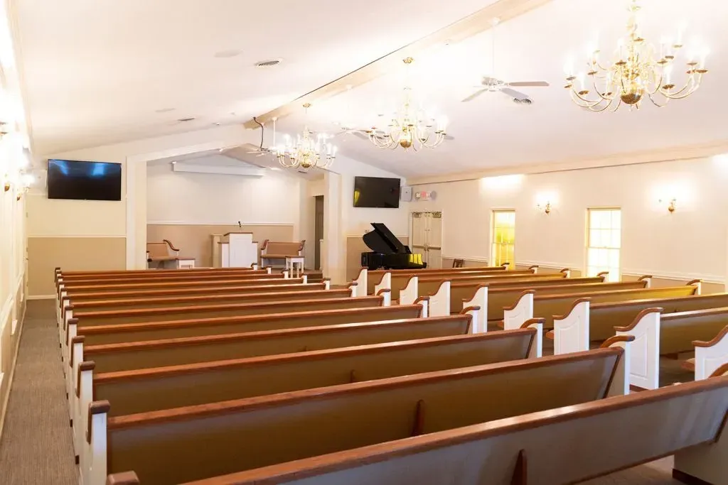 Interior of a church with rows of wooden pews, a stage, and a grand piano.