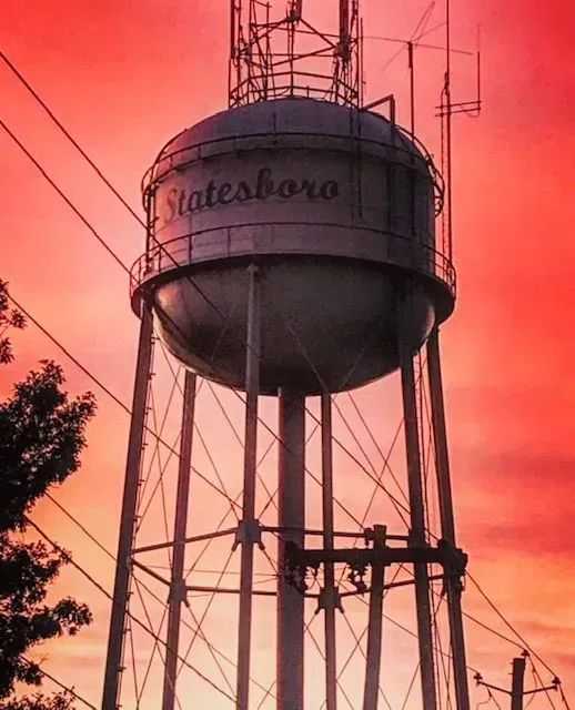 Statesboro water tower silhouetted against a vibrant red and orange sunset.