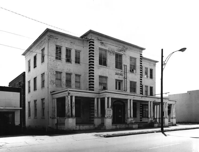 Three-story, white building with a porch and columns; the sign reads 