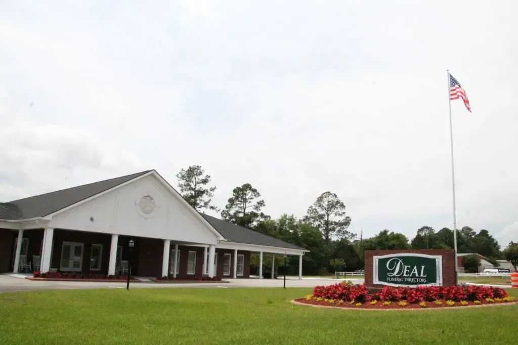 Building with sign and US flag; green lawn with red and yellow flowers.