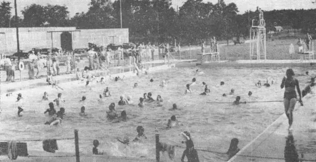 Large outdoor swimming pool crowded with people on a sunny day.