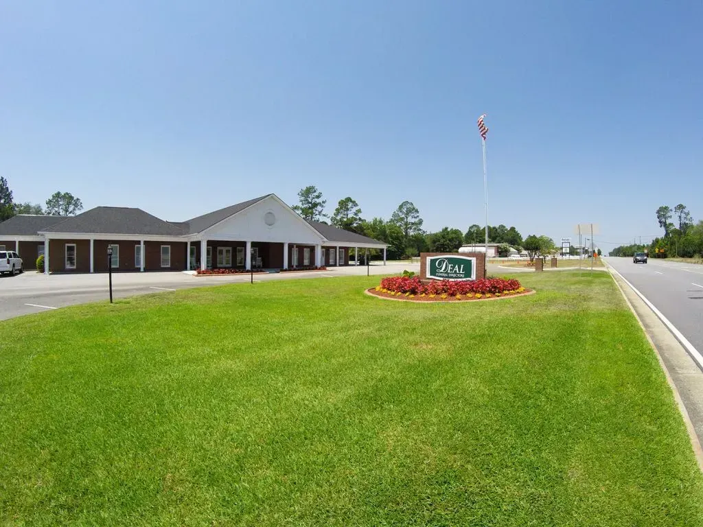 Brick building with a sign and flagpole in front of a grassy lawn, under a clear blue sky.