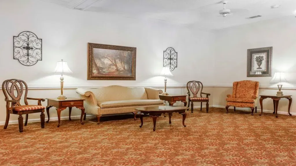 Lounge area with ornate furniture: sofa, chairs, tables, lamps, and wall art, set on patterned carpet.