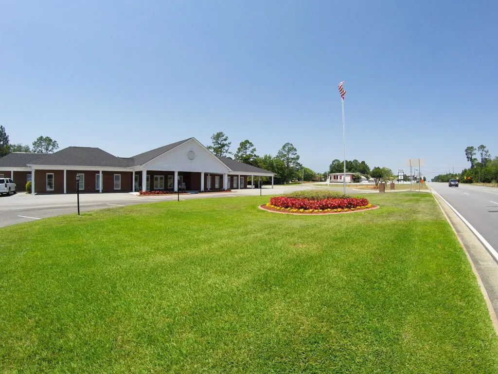 A one-story brick building with a dark roof and a flag pole on a sunny day.