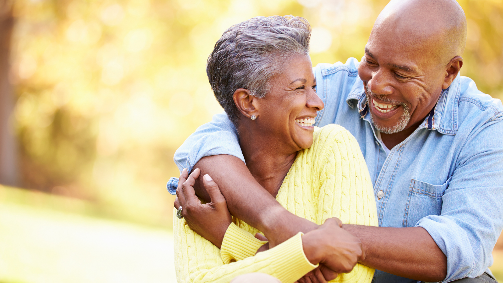 Two people smiling and hugging outdoors in warm sunlight
