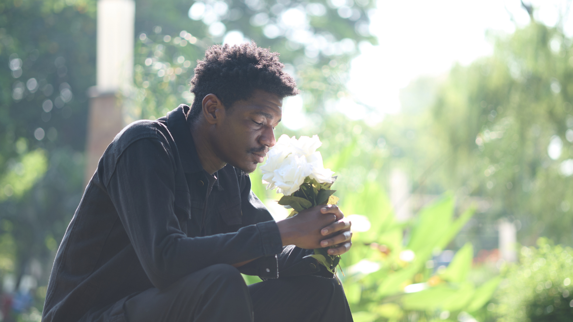 Person sitting outdoors holding a bouquet of white flowers in soft sunlight