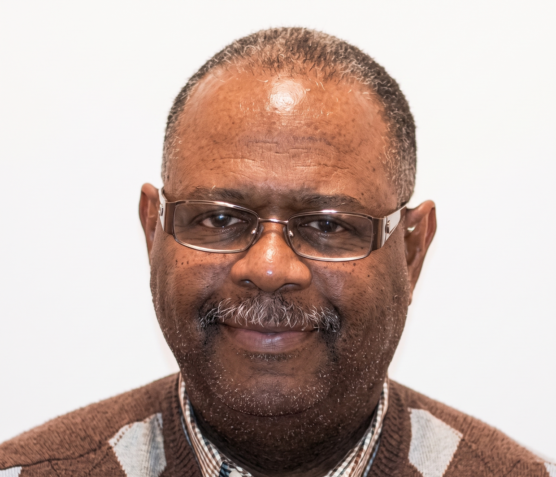 Smiling man wearing glasses and a brown sweater against a plain white background
