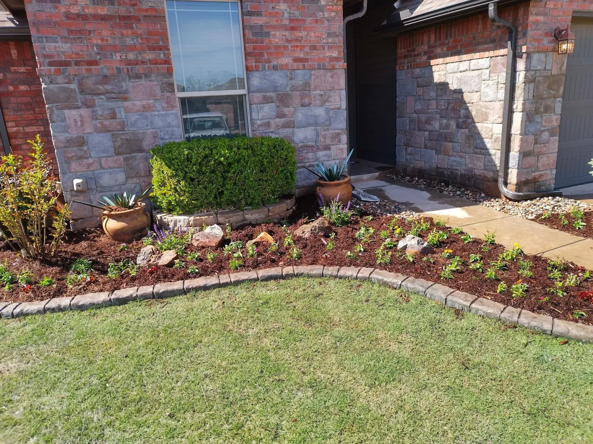Landscaped front yard with brick and stone house, green lawn, garden beds, and walkway.