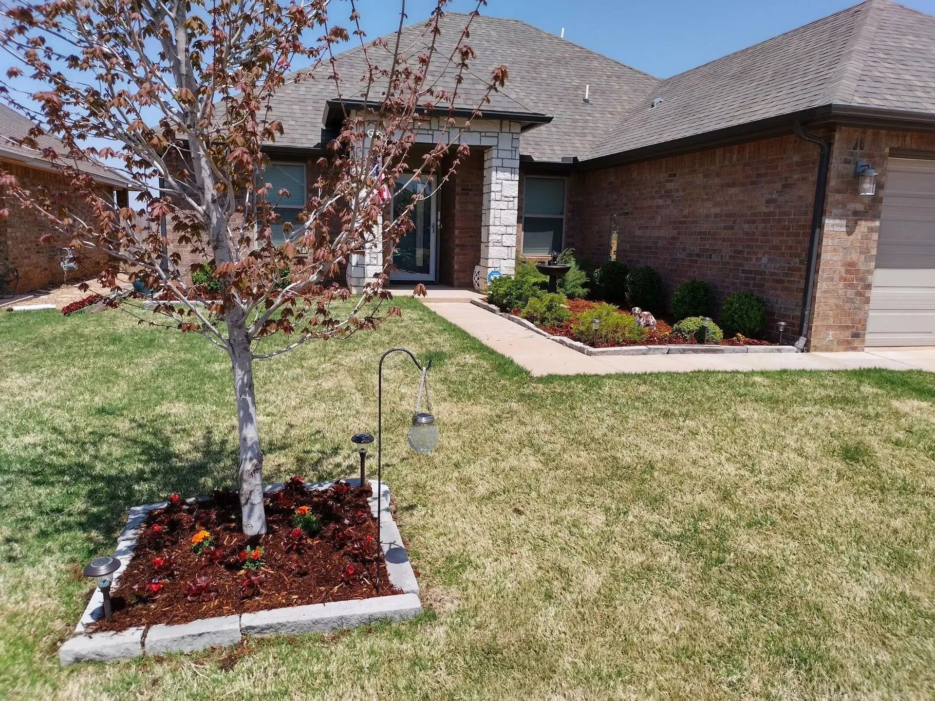 House exterior with a brick facade, green lawn, tree, and flowerbed.