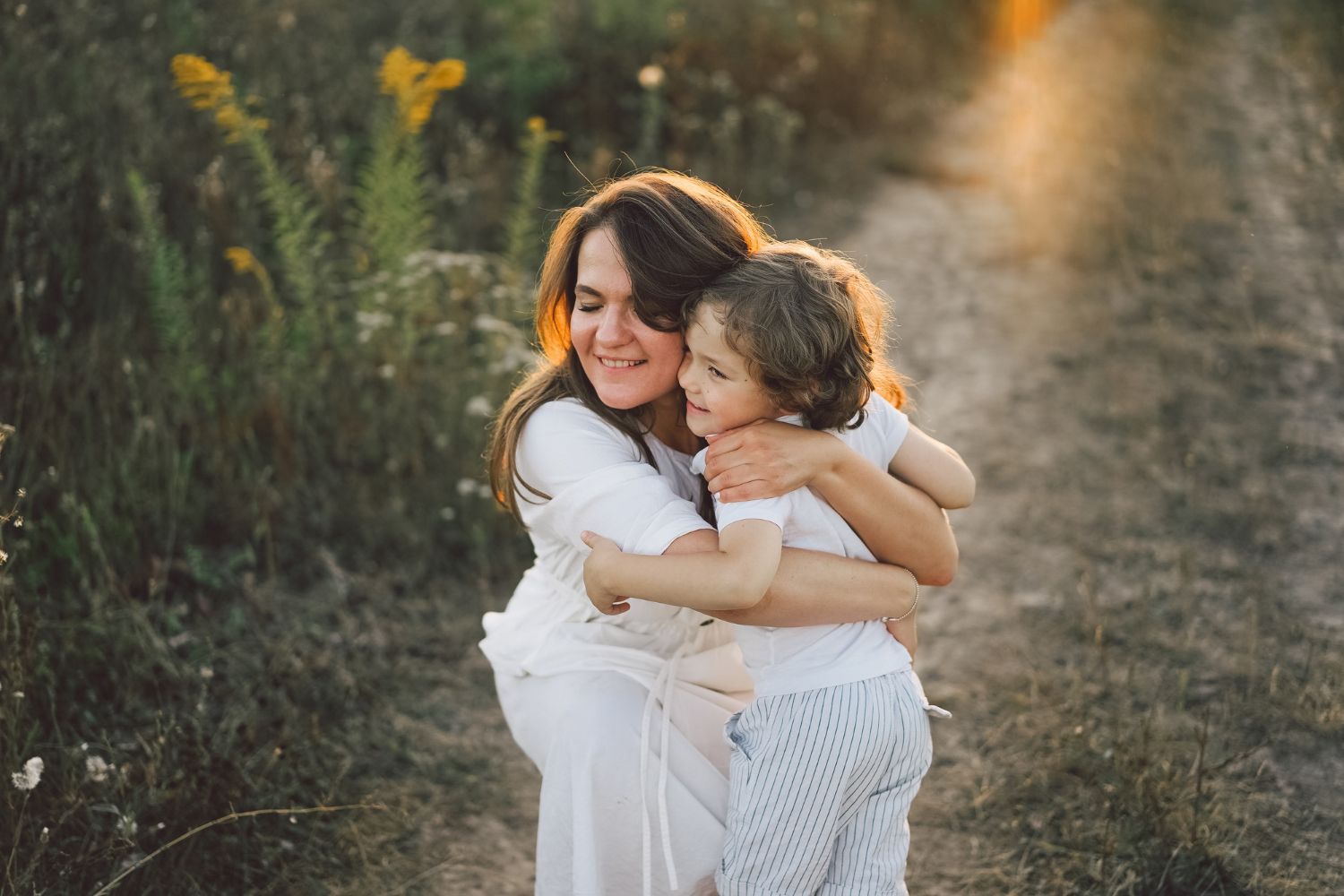 Two people hugging on a sunlit path, surrounded by greenery and soft golden light