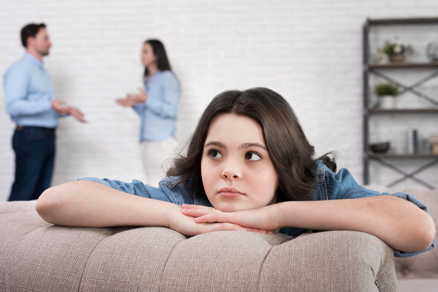 Woman resting her chin on a couch while two people talk in the blurred background