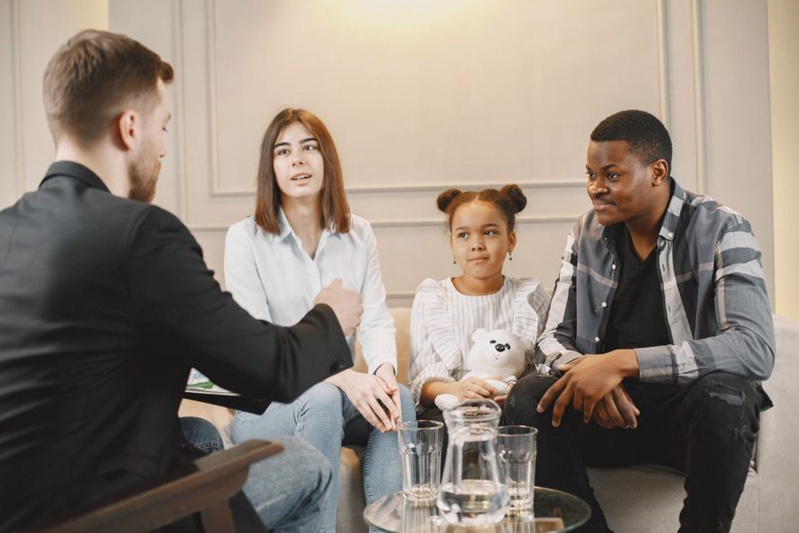Small group in a meeting room, seated around a table in a discussion with a counselor.