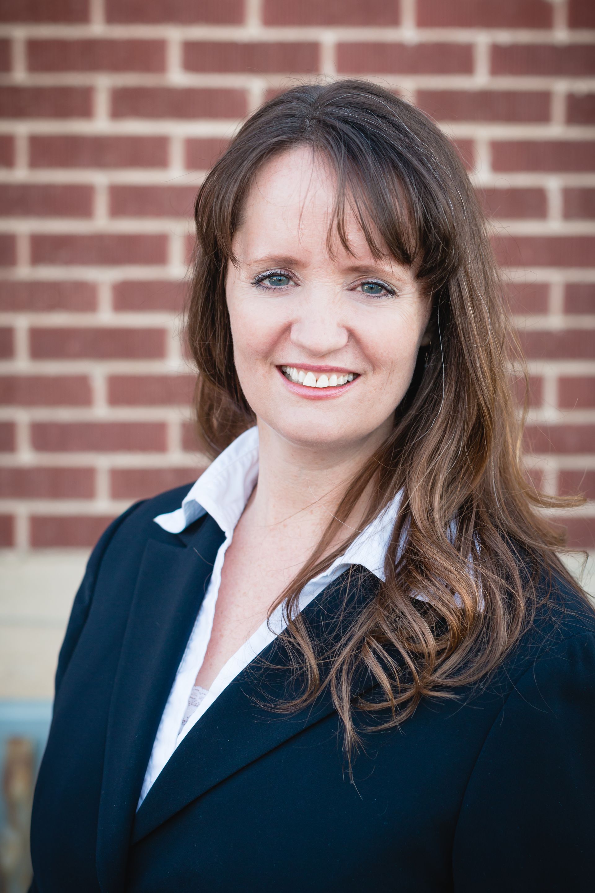 Portrait of a smiling professional in a navy blazer against a brick wall