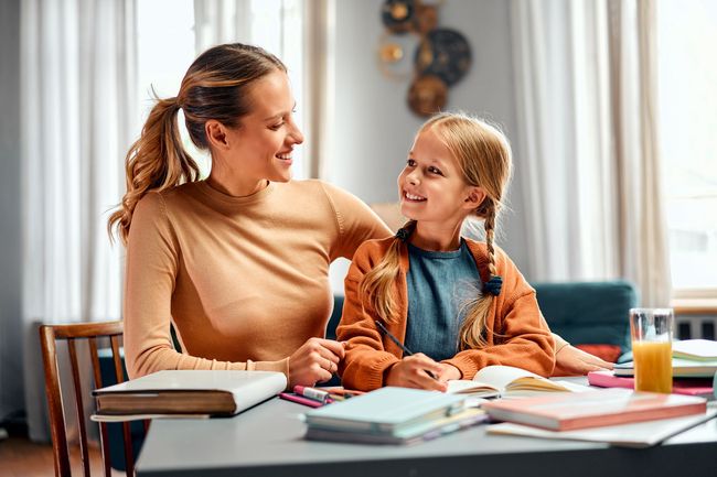 Woman and child smiling at a table with books and papers in a bright room