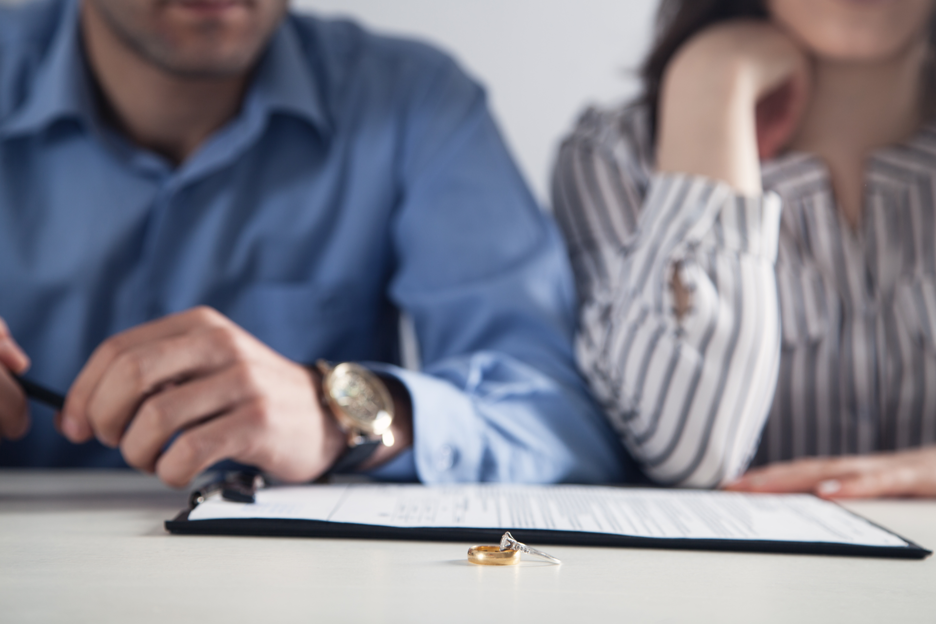 Two people signing a document at a desk, with a pen and folder in the foreground